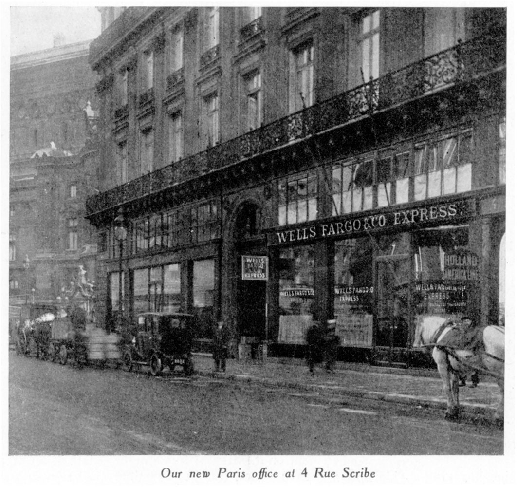 Photo of multi-story building on busy urban street. Sign reads Wells Fargo & Co. Express. Horses, wagons, autos, and people are at curb and on sidewalks. Caption at bottom reads Our new Paris office at 4 Rue Scribe. Image is black and white.