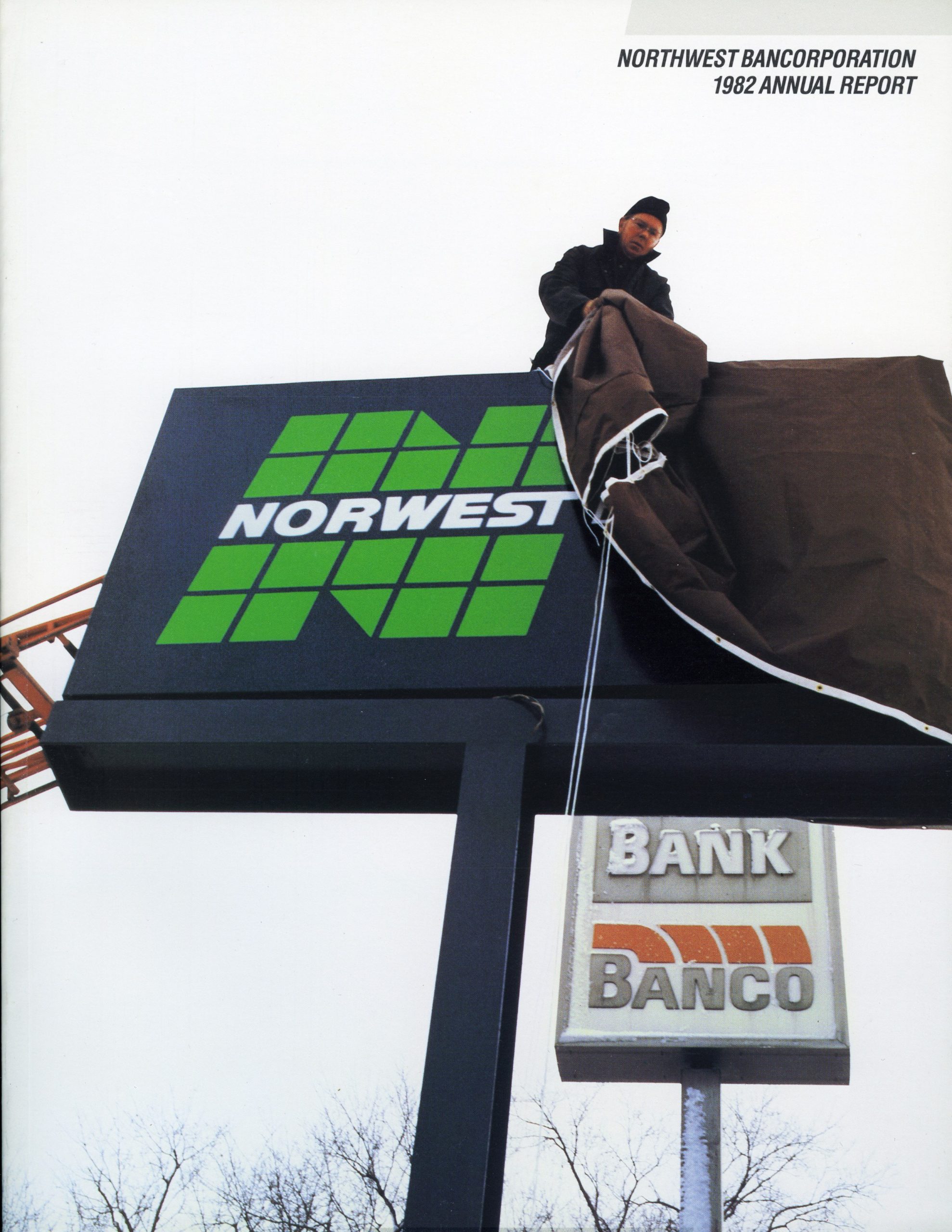 Magazine cover reads Northwest Bancorporation 1982 Annual Report. Shows man removing cover from a newly installed sign that reads Norwest in a big green letter N. In background is retired brown sign reading Banco