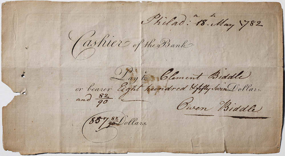 Faded blue paper reads in print Cashier of the Bank pay to. Handwritten entry names Clement Biddle and sum of eight hundred fifty seven dollars plus fraction of cent. Signed Owen Biddle. Handwritten date upper right Philad[elphia] 18 May 1782.