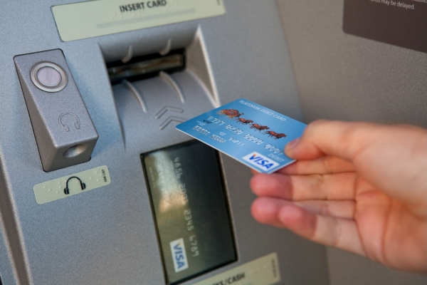 Hand inserting ATM card into machine. At left is headphone jack for ATM audio. Image is color.
