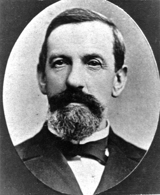 Head and shoulders portrait of Caucasian man in suit and bow tie. Man has dark hair, mustache and goatee beard, looking slightly right. Image is black and white.