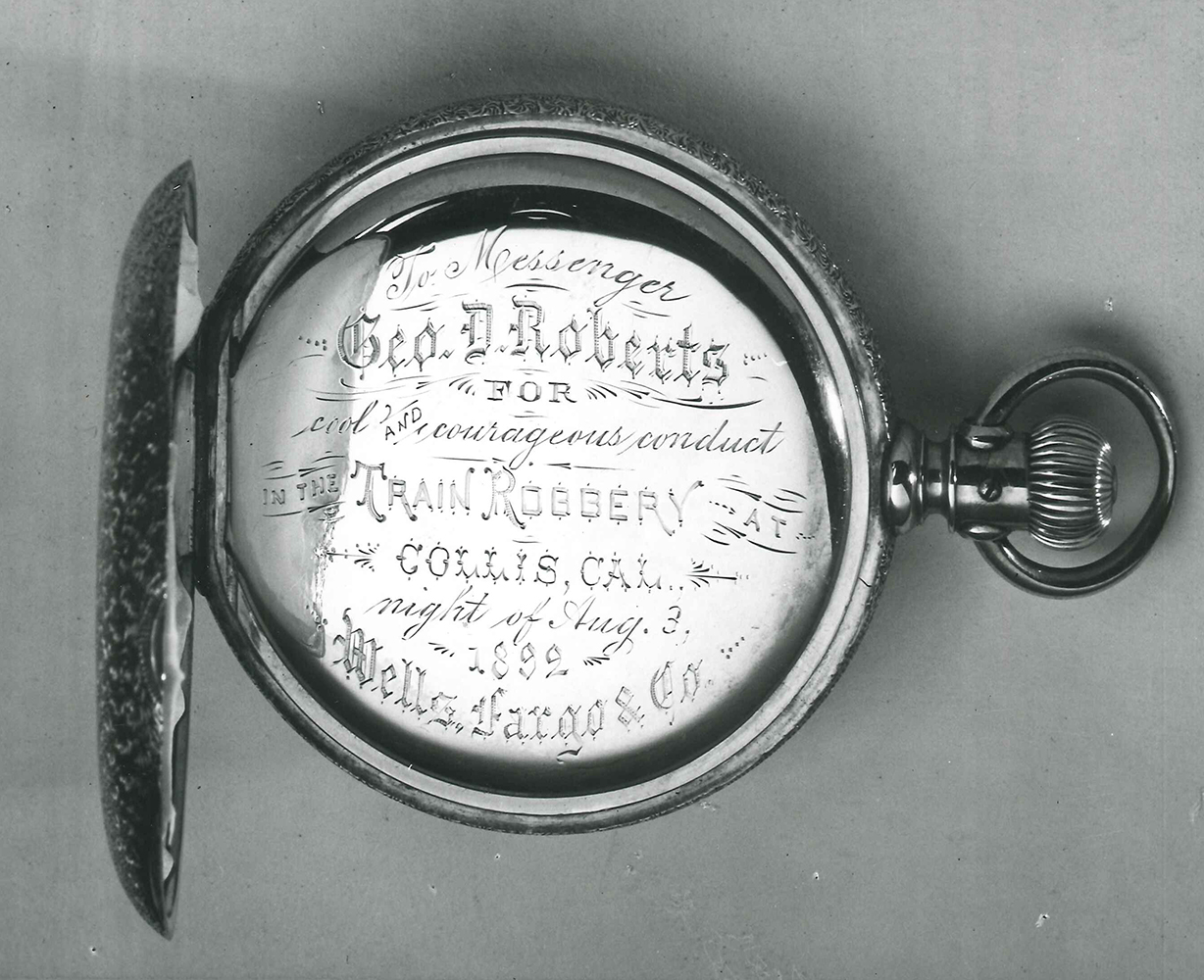 Photo of pocket watch. Engraving on cover reads: to messenger George D. Roberts for cool and courageous conduct in the train robbery at Collis, California night of August 3, 1892 Wells Fargo & Co. Image is black and white.