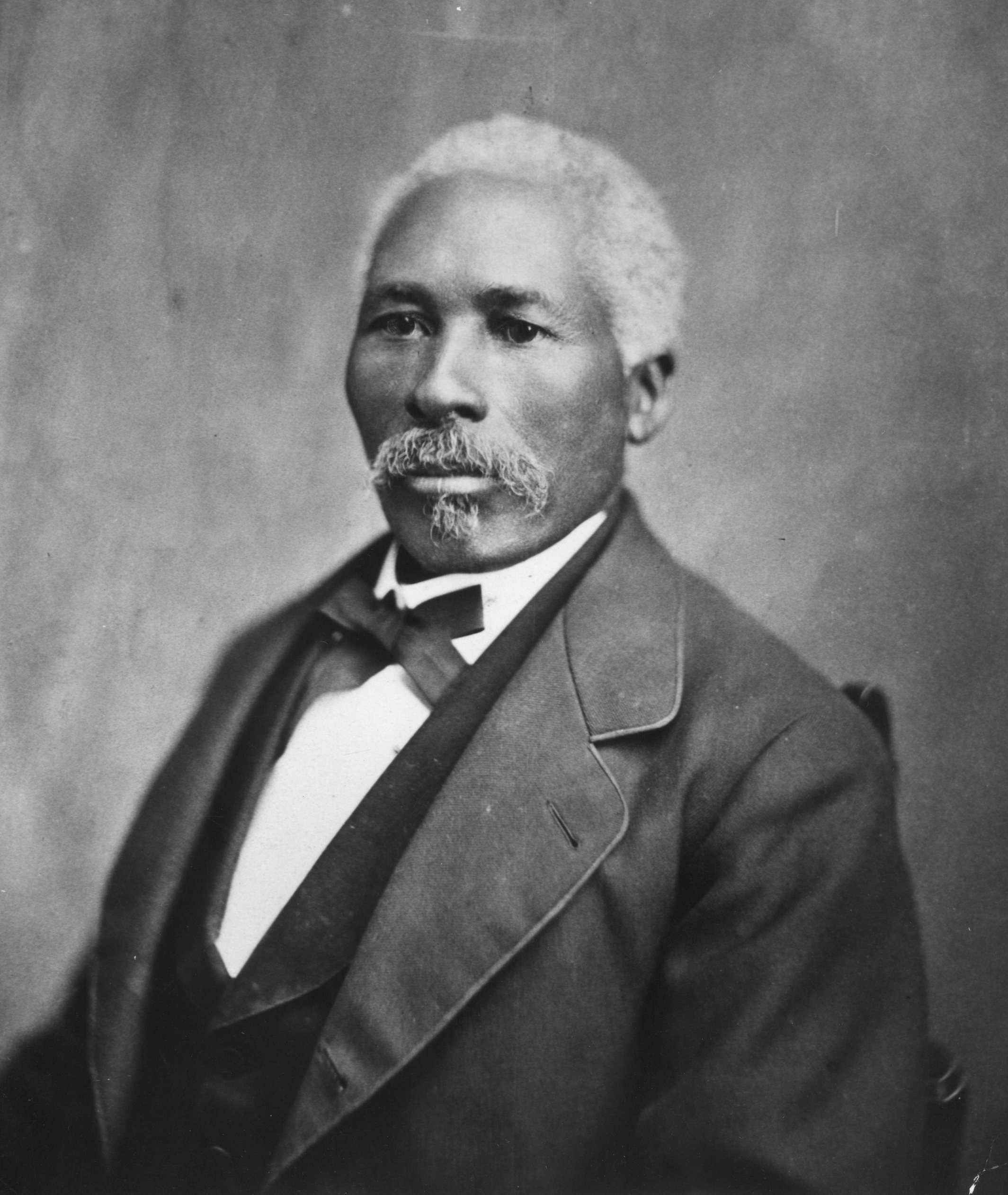 Portrait of African American man with grey hair, dressed in suit and tie. Image in black and white.