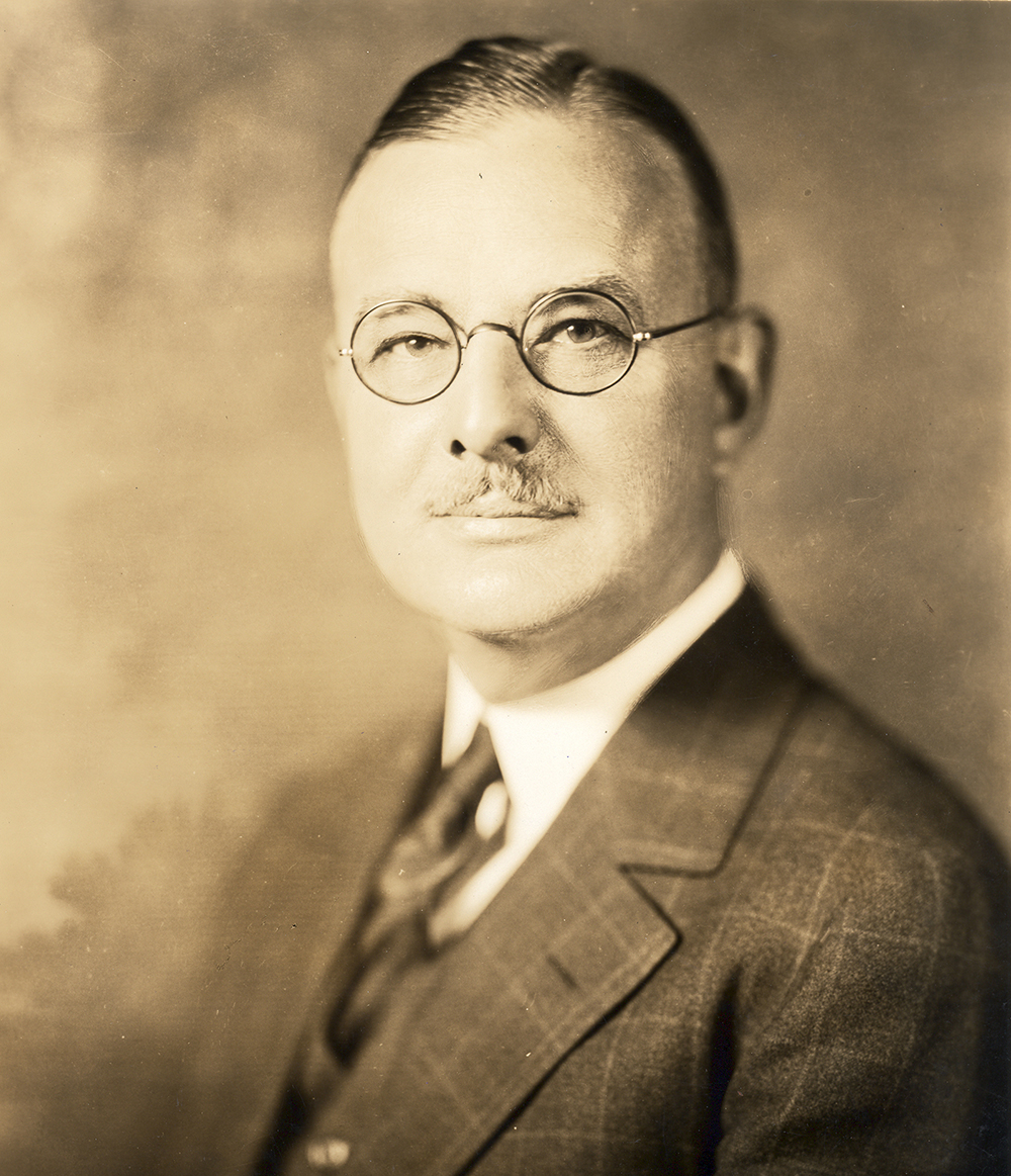 Portrait of Caucasian man wearing glasses, dressed in suit and tie. Image in black and white.