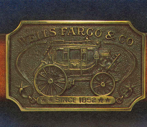 A bronze belt buckle featuring a Wells Fargo stagecoach with Wells Fargo & Co above, and since 1852 beneath.