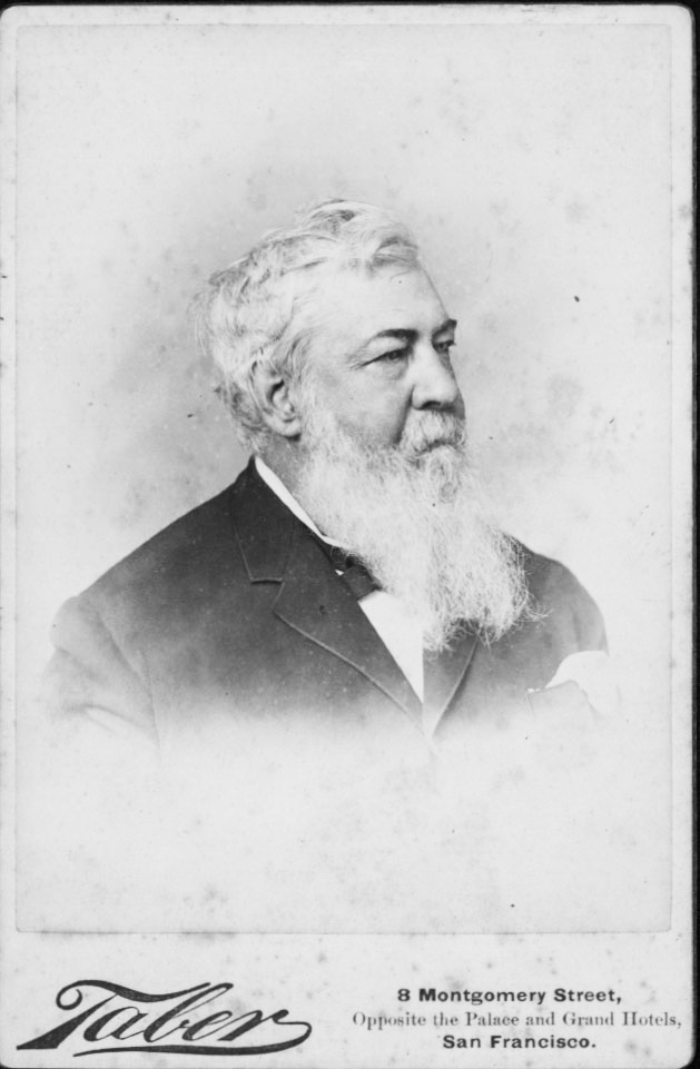 A man with a long beard in a suit looks to the right in a black and white photograph portrait.