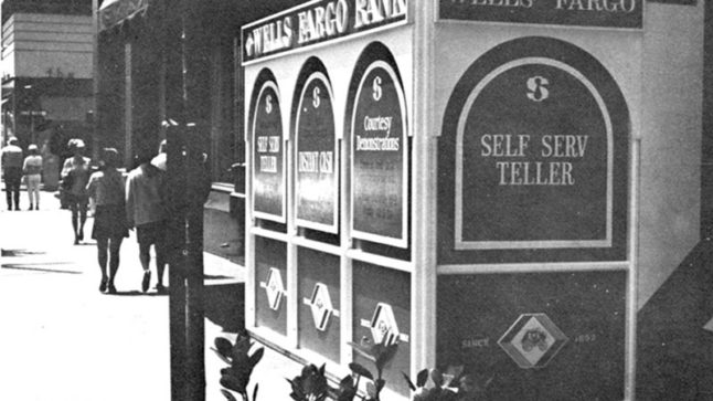 A street scene with pedestrians walking past a large box on the sidewalk. Signage on the unit says Wells Fargo Bank Self Serve Teller. Image link will enlarge image.