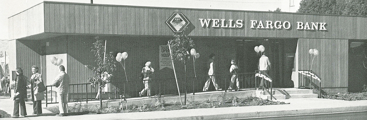 People gather outside a one-story Wells Fargo branch decorated with several balloon bunches.