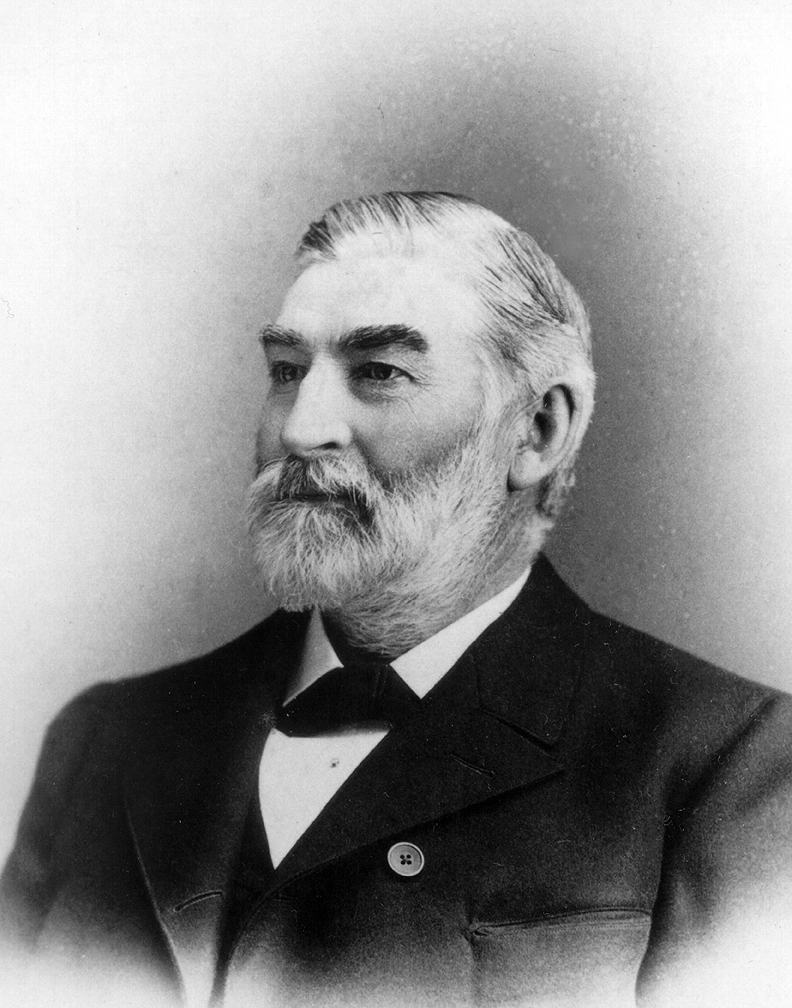 A black and white portrait of bearded man in suit. He is looking off to the side.