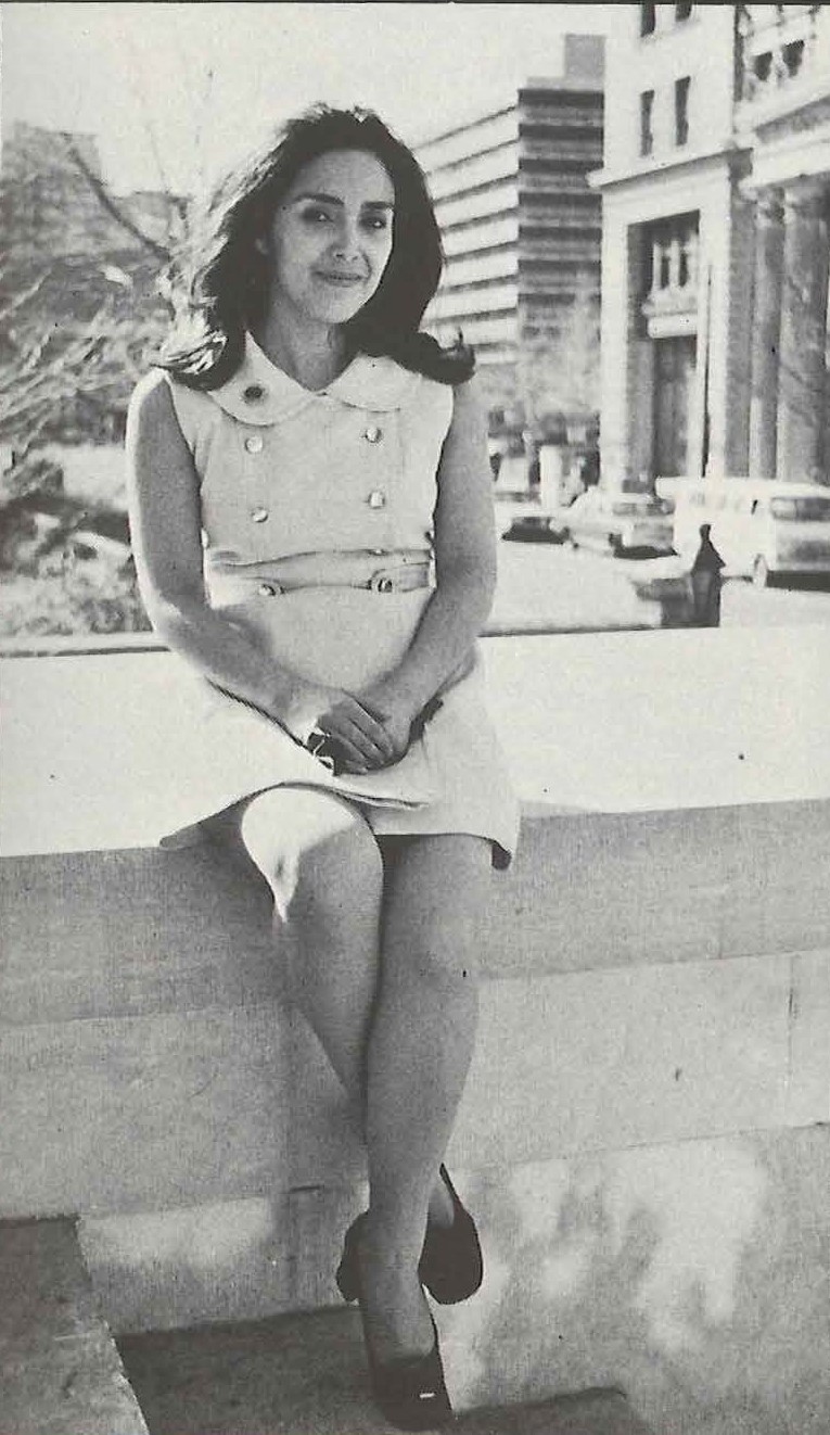 Black and white picture of a woman sitting on concrete platform next to staircase with city in the background. Image link will enlarge image.