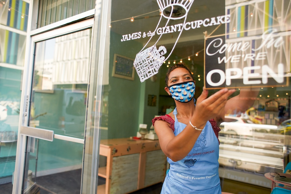 Smiling woman opens door to flower store and places open sign on window. 