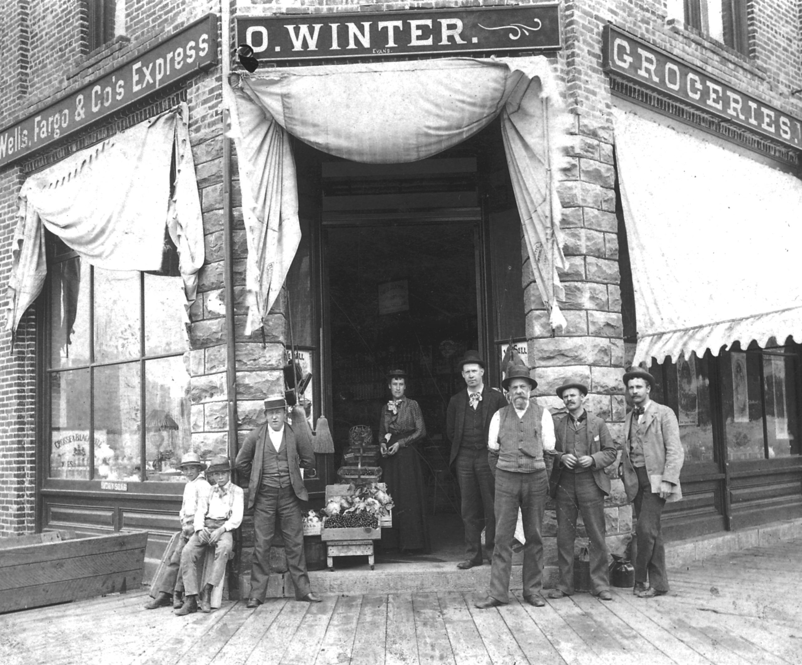 Group of people gather before the open doors of a store. A woman stands in the doorway.
