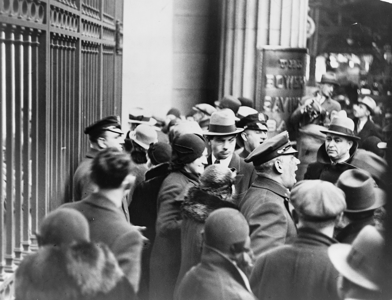 Policemen try to control a crowd of people during a bank run. On the left closed iron doors to the bank are visible. Image link will enlarge image.