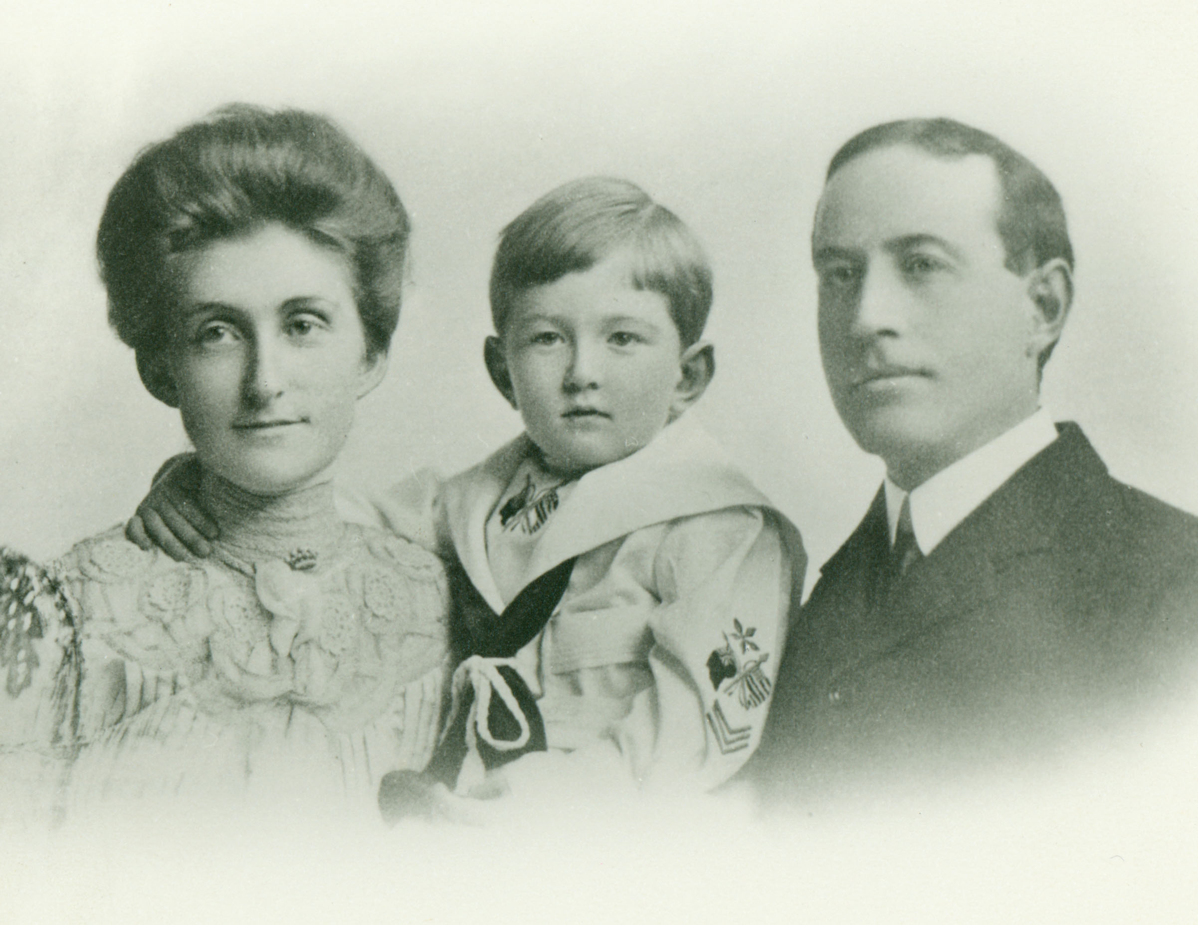 Family portrait of a woman holding a young boy standing next to a man in a suit.