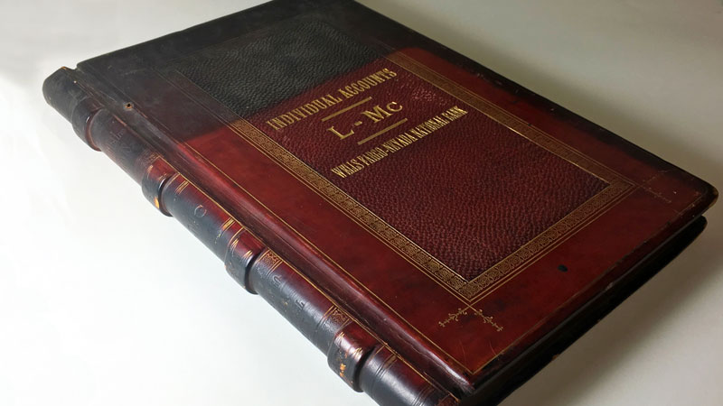 A red ledger book with black burn marks on top portion and along binding. Gold lettering reads: Individual Accounts L-Me. Image link will enlarge image.