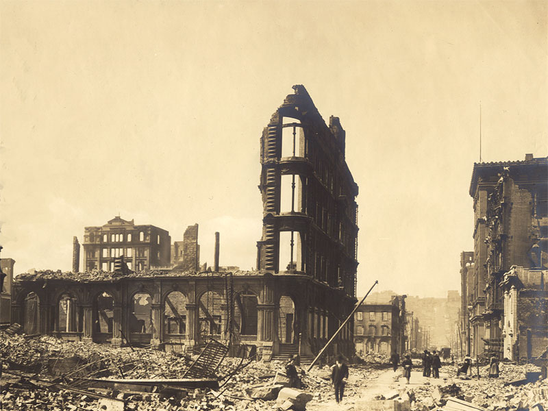 The destroyed remains of the Nevada National Bank building. Only the framing of the main entrance remains intact, showing four floors of windows. Rubble from the rest of the building litters the street. Image link will enlarge image.