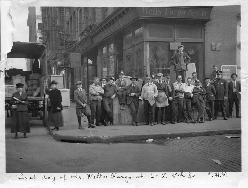 People gather on a New York City street in front of a Wells Fargo office building in 1918. A sign on the building reads: Wells Fargo & Co. Black and white image. Image link will enlarge image.