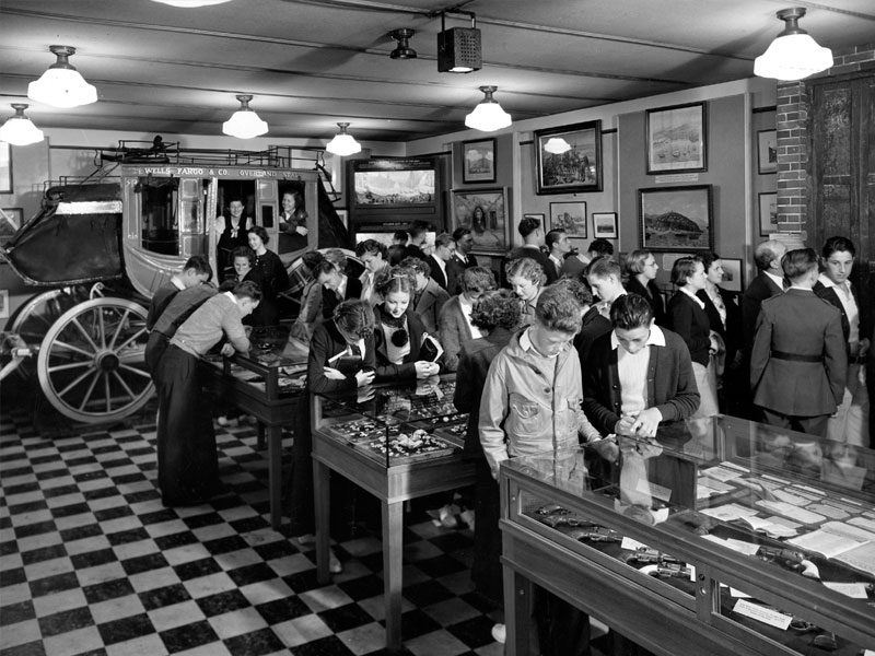 Museum visitors interact with displays in 1936. The floor is tiled in black and white in the foreground while a stagecoach is displayed in the background. Image link will enlarge image.
