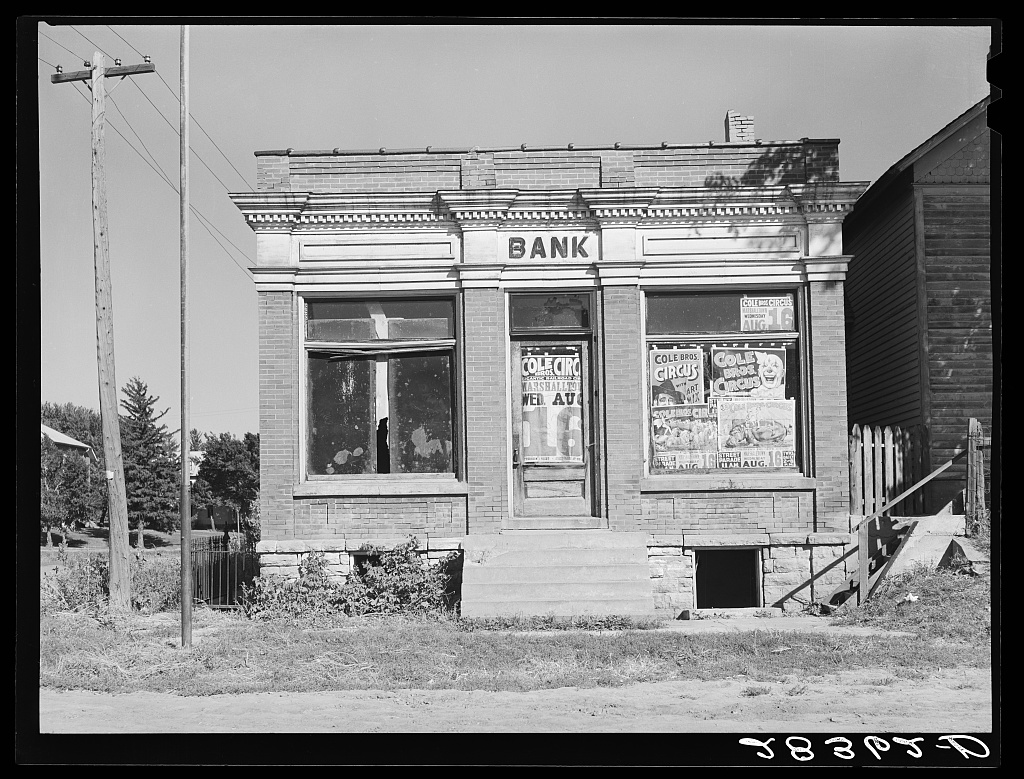 A small, dilapidated building with the word Bank over the entrance. In the window are ads for a circus. Image link will enlarge image.