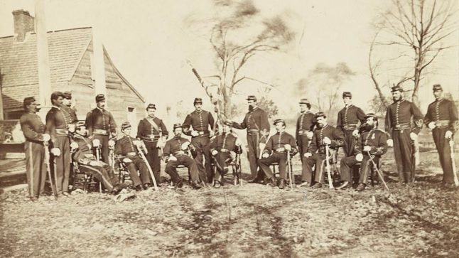 Officers of Buffalo's 164th New York Infantry pose holding their weapons in a field during the Civil War. Black and white historic photograph. Image link will enlarge image.