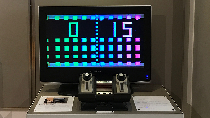 A box TV with dials connected to a home Atari gaming system. The TV monitor is displaying a game with a green and a red player divided by a blue separated line.
