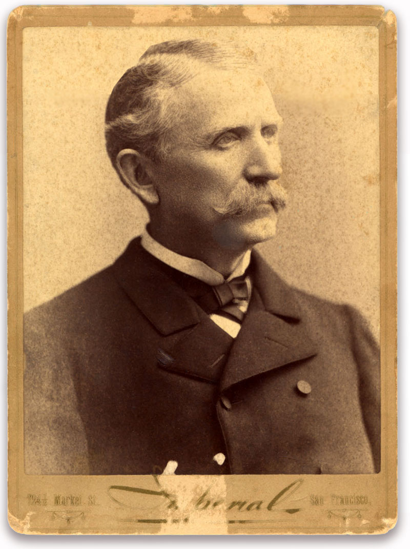 A yellowed photocard of a man with grey hair and mustache wearing a black suit coat and bow tie.