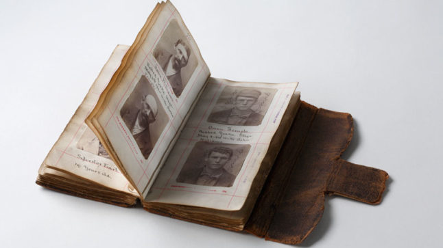 An aged, leather-bound book, opened to two pages with two headshots on each page with handwritten notes on the page.