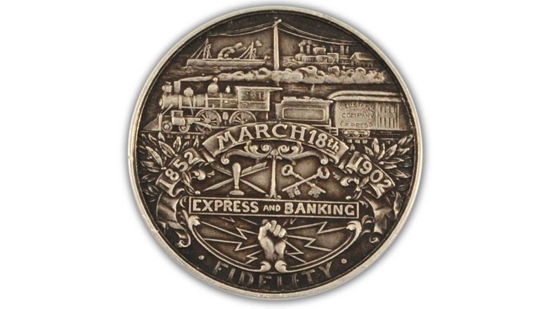A commemorative coin inscribed with the date March 18th, 1852, Express and Banking. Engraved into the coin are a collection of images including a steam train, telegraph lines and a bank stamp and keys.