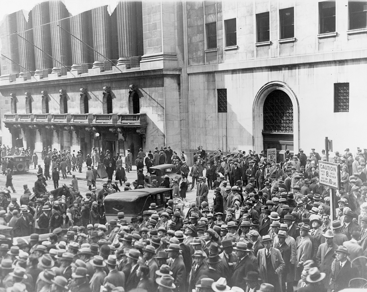 A large crowd of people crowd the street in the foreground. In the background is the New York Stock exchange building. Image link will enlarge image.