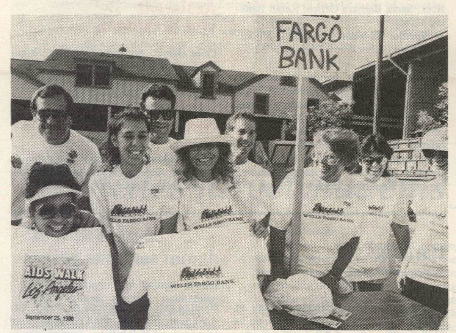 Group of people wearing Wells Fargo shirts gather outside. Part of a sign is visible reading: Fargo Bank. One person holds up a shirt that reads: AIDS Walk Los Angeles.